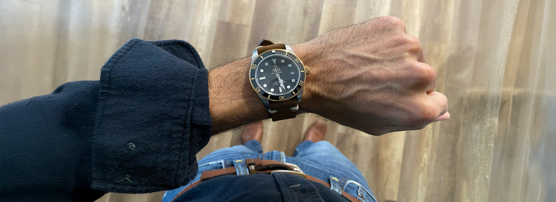 A black watch on a man's wrist with a wood floor background.