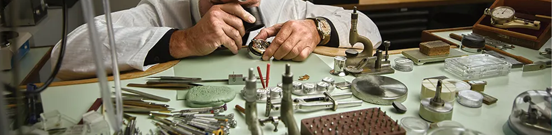 A watchmaker inspects a movement at his work bench.