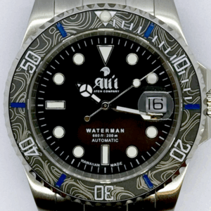 A close up of the dial on the Ali'i Watch Company Waterman watch with black dial and black carbon fiber bezel with blue minute markers.