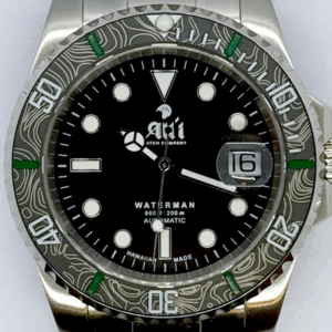 A close up of the dial on the Ali'i Watch Company Waterman watch with black dial and black carbon fiber bezel with green minute markers.