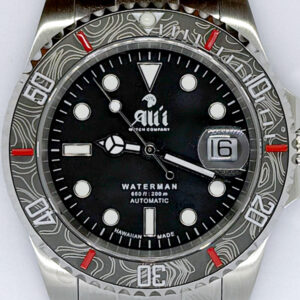 A close up of the dial on the Ali'i Watch Company Waterman watch with black dial and black carbon fiber bezel with red minute markers.