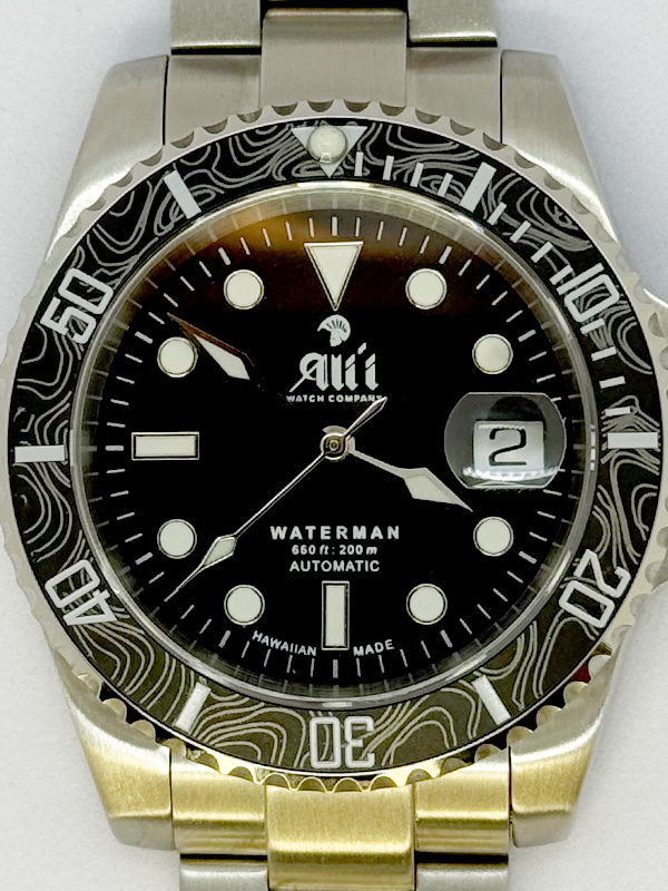 A close up of the dial on the Ali'i Watch Company Waterman watch with black dial and black carbon fiber bezel with silver minute markers.