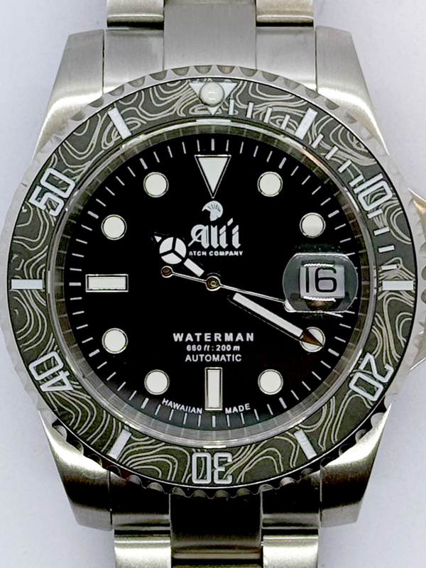A close up of the dial on the Ali'i Watch Company Waterman watch with black dial and black carbon fiber bezel with silver minute markers.