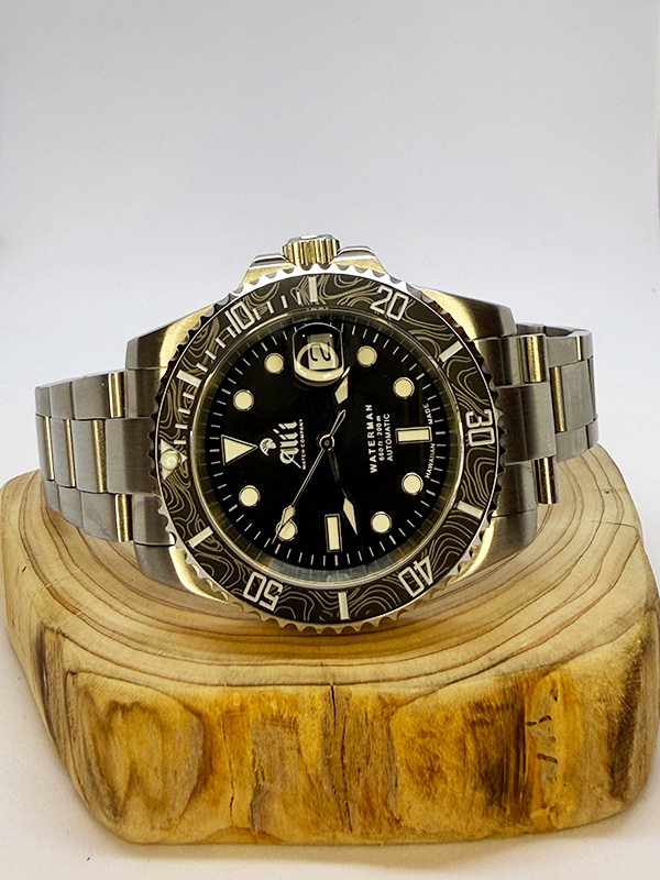 Ali'i Watch Company Waterman watch with a black bezel and carbon fiber bezel with silver minute markers sits on a piece of wood.